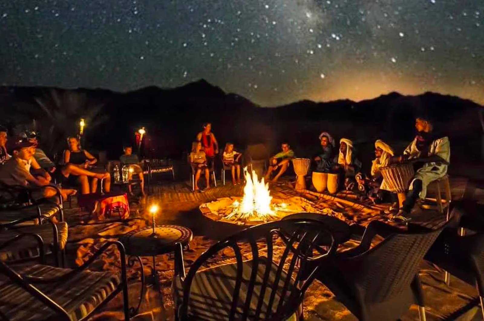 Christmas in Morocco — family tours, Sahara and blue-city escapes Travellers and Berber musicians sit around a campfire under a star-filled sky at a Sahara desert camp
