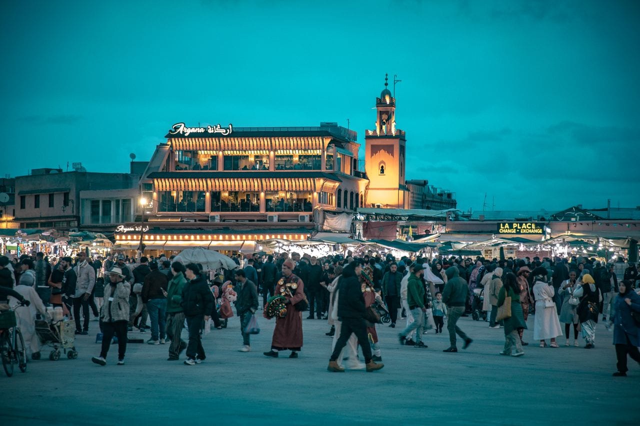 Crowds fill Jemaa el-Fnaa square in Marrakech at dusk beside lit food stalls