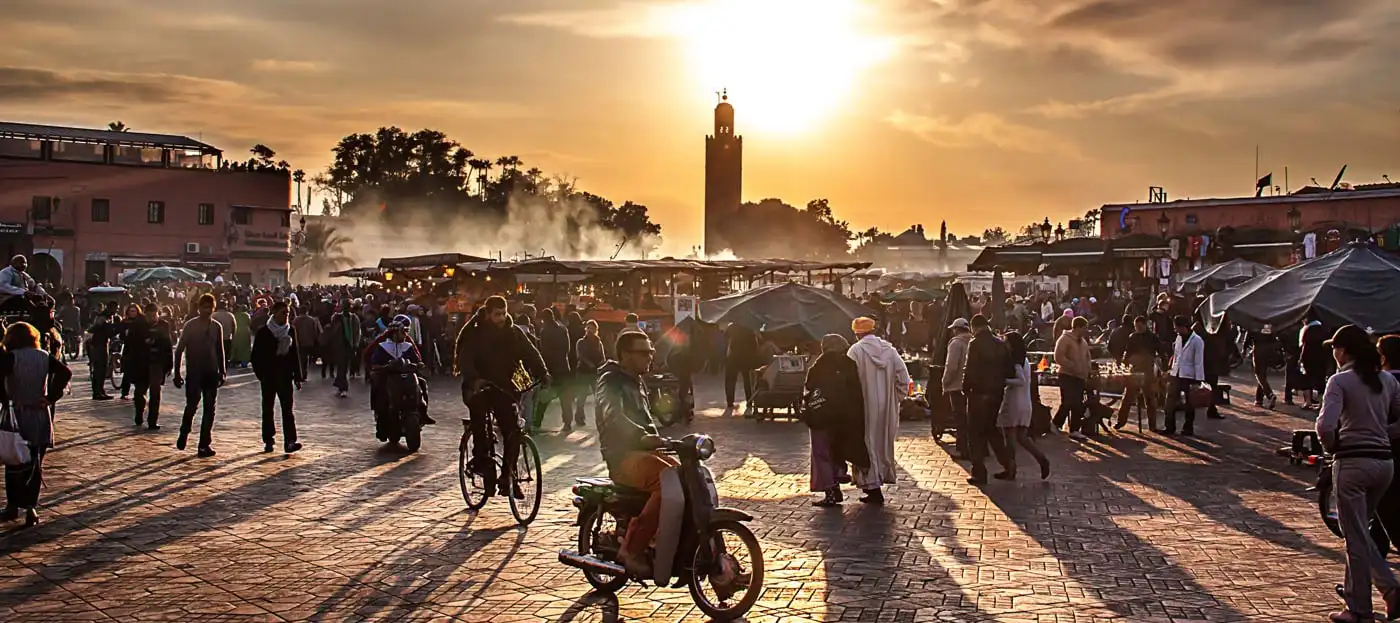 Jemaa el-Fna square in Marrakech at sunset with food stalls, crowds and the Koutoubia minaret behind