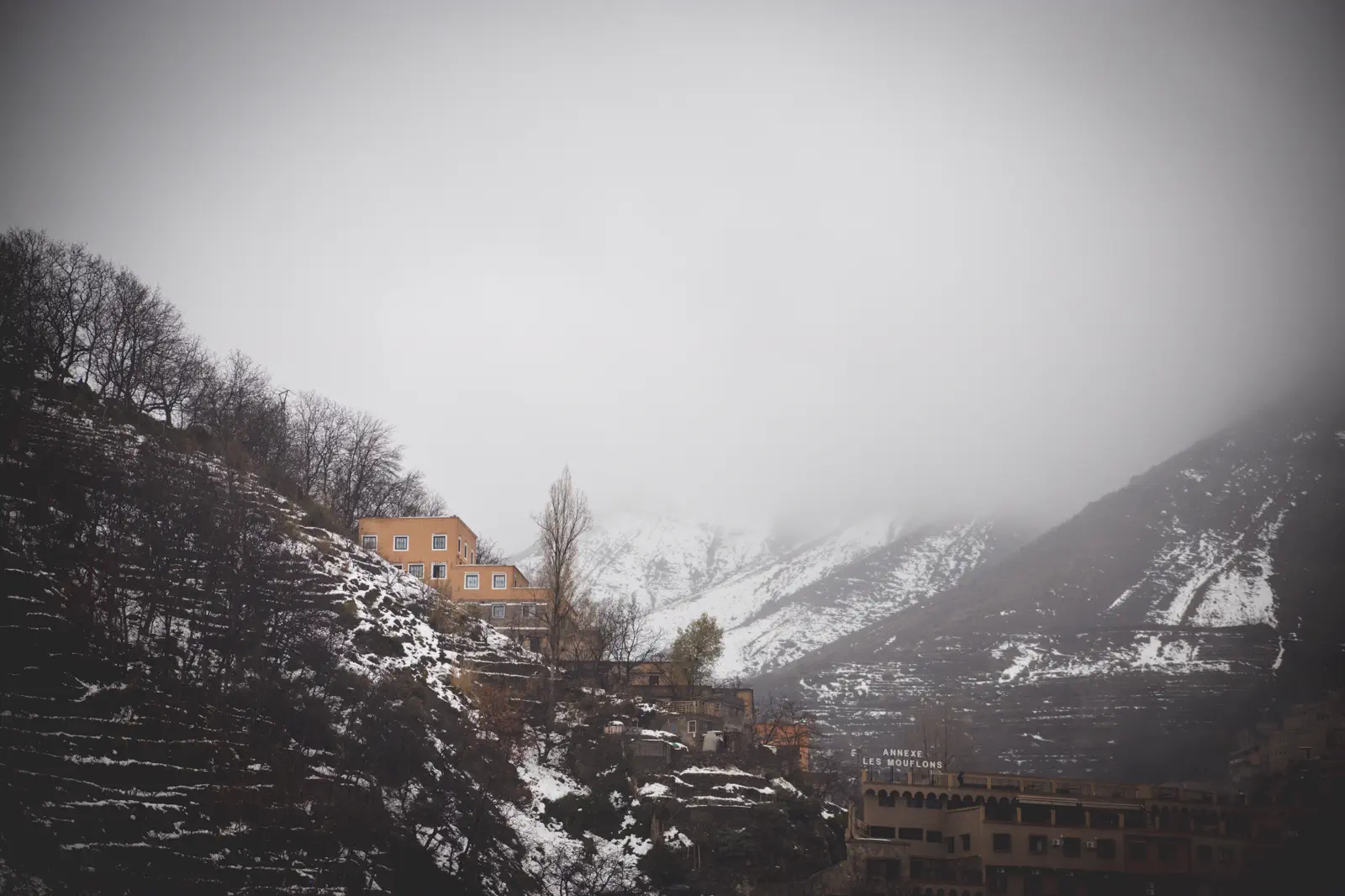 Snow-covered Atlas Mountain village above Imlil in winter, with terraced hillsides and guesthouses