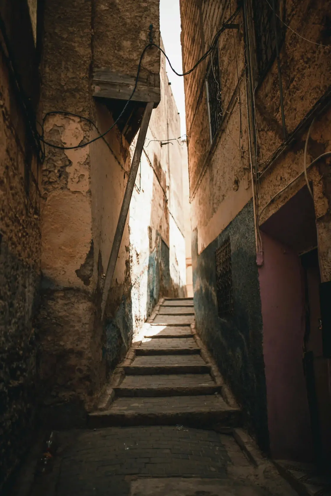 Narrow sunlit alleyway climbing worn stone steps through the Fes medina — slow travel with Local Morocco Tours