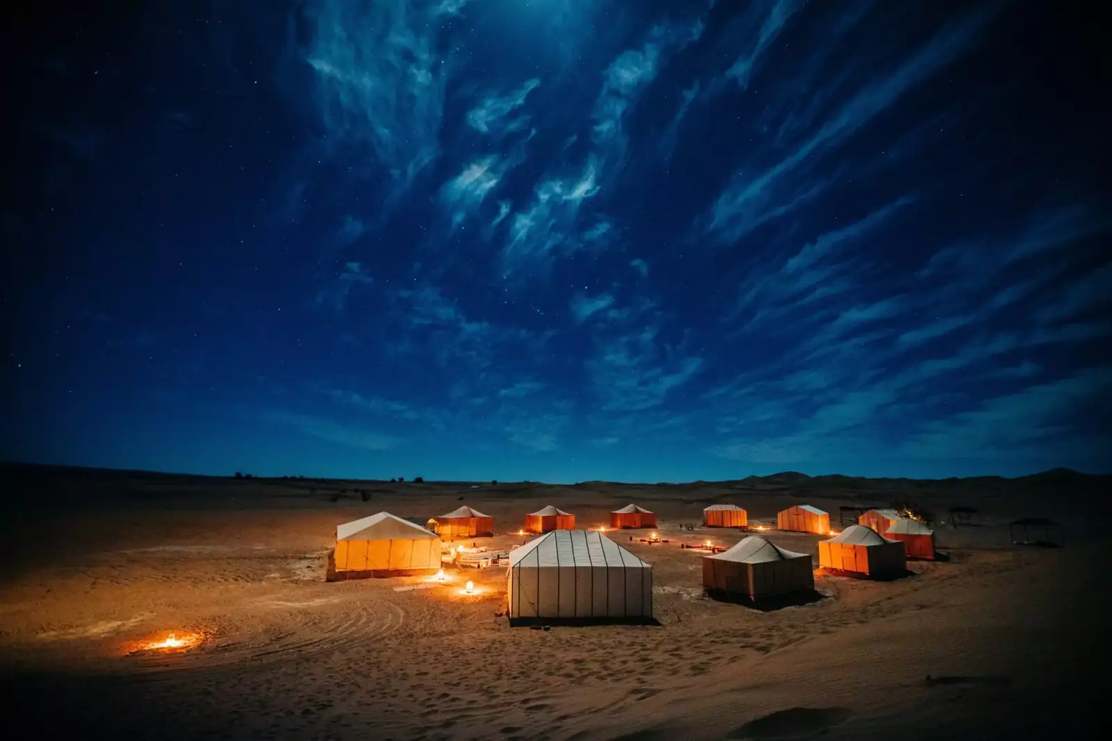Luxury desert camp glowing amber beneath a starry Sahara sky near Merzouga — overnight desert tours in Morocco
